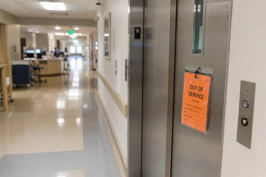 Orange out-of-service tag on stainless steel hospital elevator doors in a Southern California healthcare facility following a failed California elevator inspection