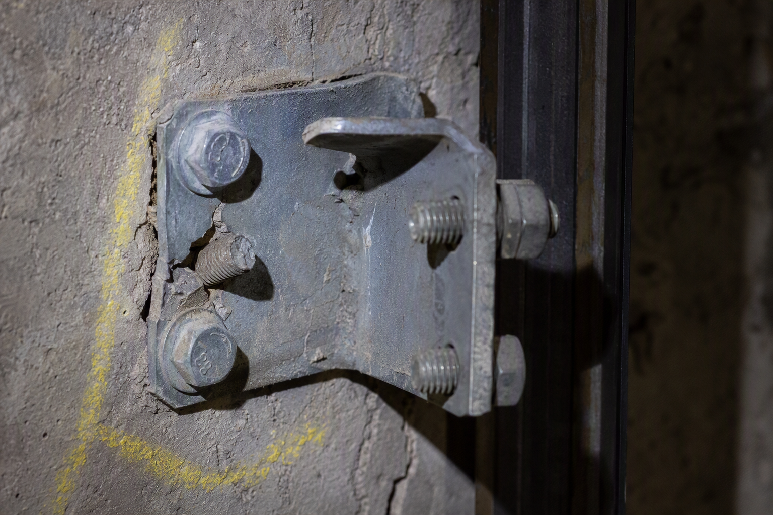Close-up of a sheared guide rail bracket anchor bolt inside a California elevator hoistway, a common seismic damage finding requiring repair before elevator re-inspection