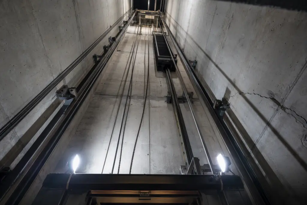 Inside view of a California commercial elevator hoistway after a seismic event, showing misaligned guide rails and displaced counterweight requiring post-earthquake inspection